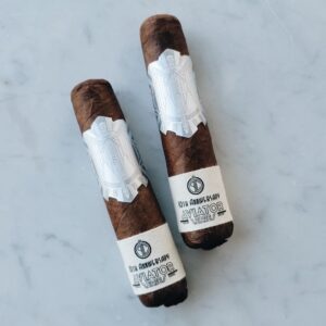 Two Principle Aviator 10th Anniversary cigars with white angel band labels and dark brown wrappers on marble background.
