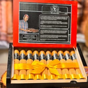 Open box of Gomez Lopez Connecticut Toro cigars with yellow ribbon, featuring portrait and legacy information on red lid.