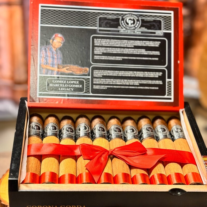 Gomez Lopez Maduro Toro cigars in open box with red ribbon and product information card featuring cigar maker portrait.