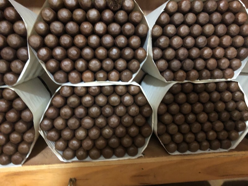 Six boxes of premium torpedo cigars with cubanofiller criollo ligero, displaying tightly rolled brown cigars arranged in white paper-lined packaging on woode…