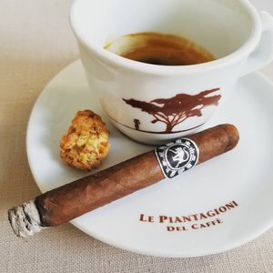 Frothy Monkey cigar paired with espresso cup and pastry on branded saucer, showcasing premium coffee and cigar pairing experience.