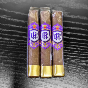 Three Royalty Robusto cigars with purple and gold bands featuring ornate crown logo displayed on textured black surface.