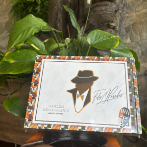 Harlem Renaissance Limited Edition cigar box with stylized portrait and geometric African-inspired border design displayed outdoors among green foliage.