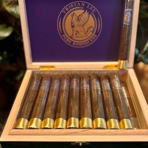 Open wooden cigar box displaying Tristan Maduro cigars with purple interior label and gold-banded cigars arranged in rows.
