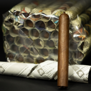 Brown premium cigar displayed with white-wrapped cigars and decorative honeycomb patterned packaging on black background.