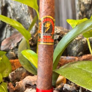 Harlem The Brother Maduro cigar with red band displayed among green foliage and weathered wood background